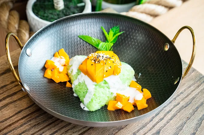 Pandan sticky rice with mango and coconut cream in a dark handled bowl